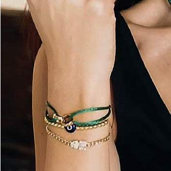 A close-up of a woman wearing a green beaded choker necklace with a round white pendant, matching green and gold bracelets on her wrist, and a gold hoop earring.